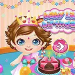 Egy kisgyermek koronával egy születésnapi torta előtt ül, körülötte színes lufikkal és ajándékokkal, háttérben baby lily birthday felirat