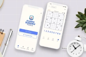 Két okostelefon egy asztalon, az egyik egy sudoku alkalmazás nyitóképernyőjét mutatja, a másik egy sudoku rejtvényt, körülöttük irodai eszközök és egy kisméretű ébresztőóra
