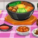 Egy asztalon különböző ázsiai ételek, köztük leves, gombóc, tofu és zöld tea egy rózsaszín kockás terítőn