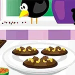 A képen négy csokis sütemény látható egy tányéron, háttérben egy ablak előtt egy fekete madár, egy reszelő, fűszerek, és csokoládé