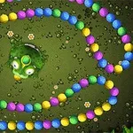 Színes golyók kígyózó vonalban egy zöld béka körül barna háttéren, növényekkel és vízcseppekkel díszítve