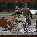 Rövid ujjú mezes férfiak sáros pályán rögbiznek, középen egy kirakós részlet látható
