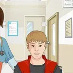 Egy kórházi folyosón egy nővér mosolyogva tol egy kerekesszékben ülő fiatal fiút