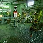 Egy futurisztikus bár belső terében robotok ülnek asztaloknál, körülvéve retro berendezésekkel és neonszivárványos világítással