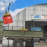 Teherautó egy rakományátvételi raktár előtt, miközben egy daru piros konténert emel