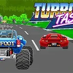 Kétsávos úton haladó kék monster truck és piros sportautó, háttérben zöld fák és nagy, színes Turbofastic felirat